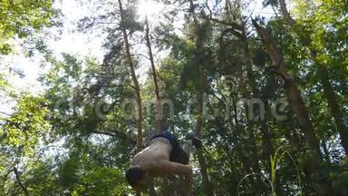 强壮的肌肉男在森林里做倒立。 肌肉男健身男在木头上做特技。 运动员
